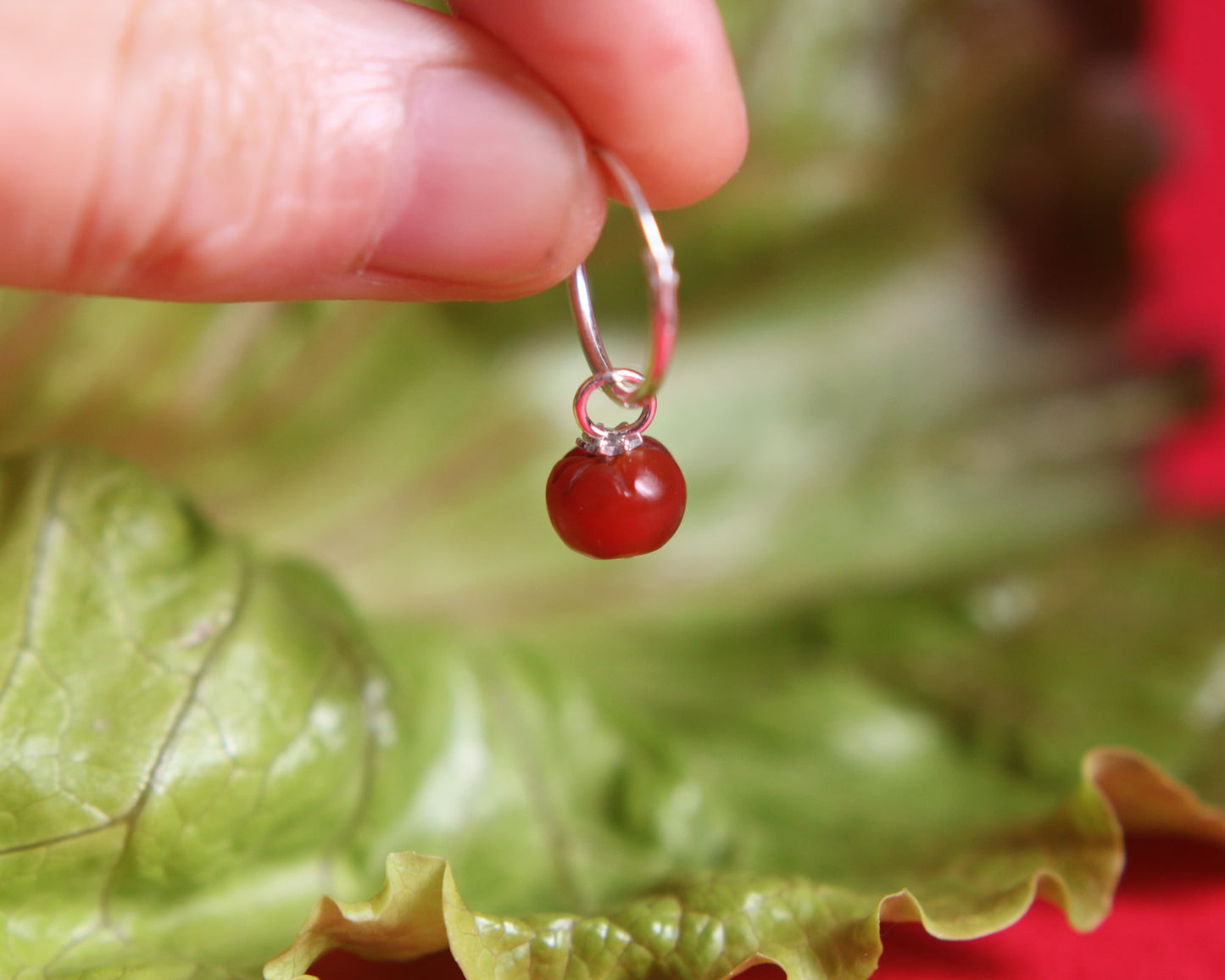 Pendentif tomate sur boucle d'oreille sur une feuille de salade sur un fond rouge