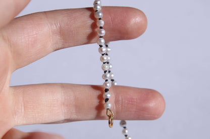 Collier en perles avec noeuds en fil de soie noir tenu sur deux doigts