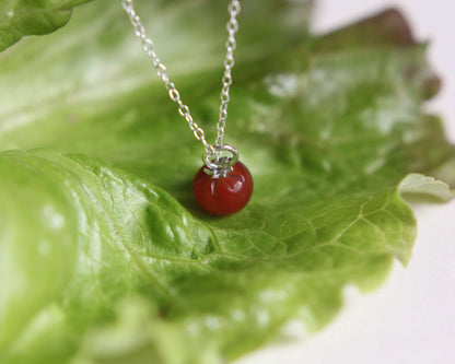Pendentif tomate sur chaine en argent posé sur une feuille de salade sur un fond blanc