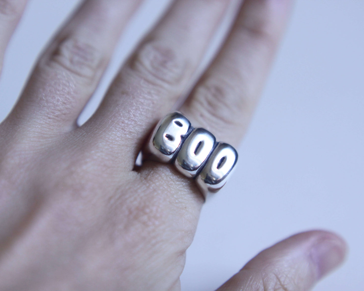 zoom sur une bague en argent figurant l'expression "BOO" portée au doigt