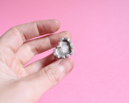 une main tient une bague en argent représentant un château fort en forme de coeur