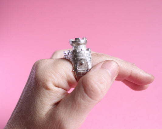 vue de profil d'une bague en argent en forme de château fort avec une tour et un pont levis fermé