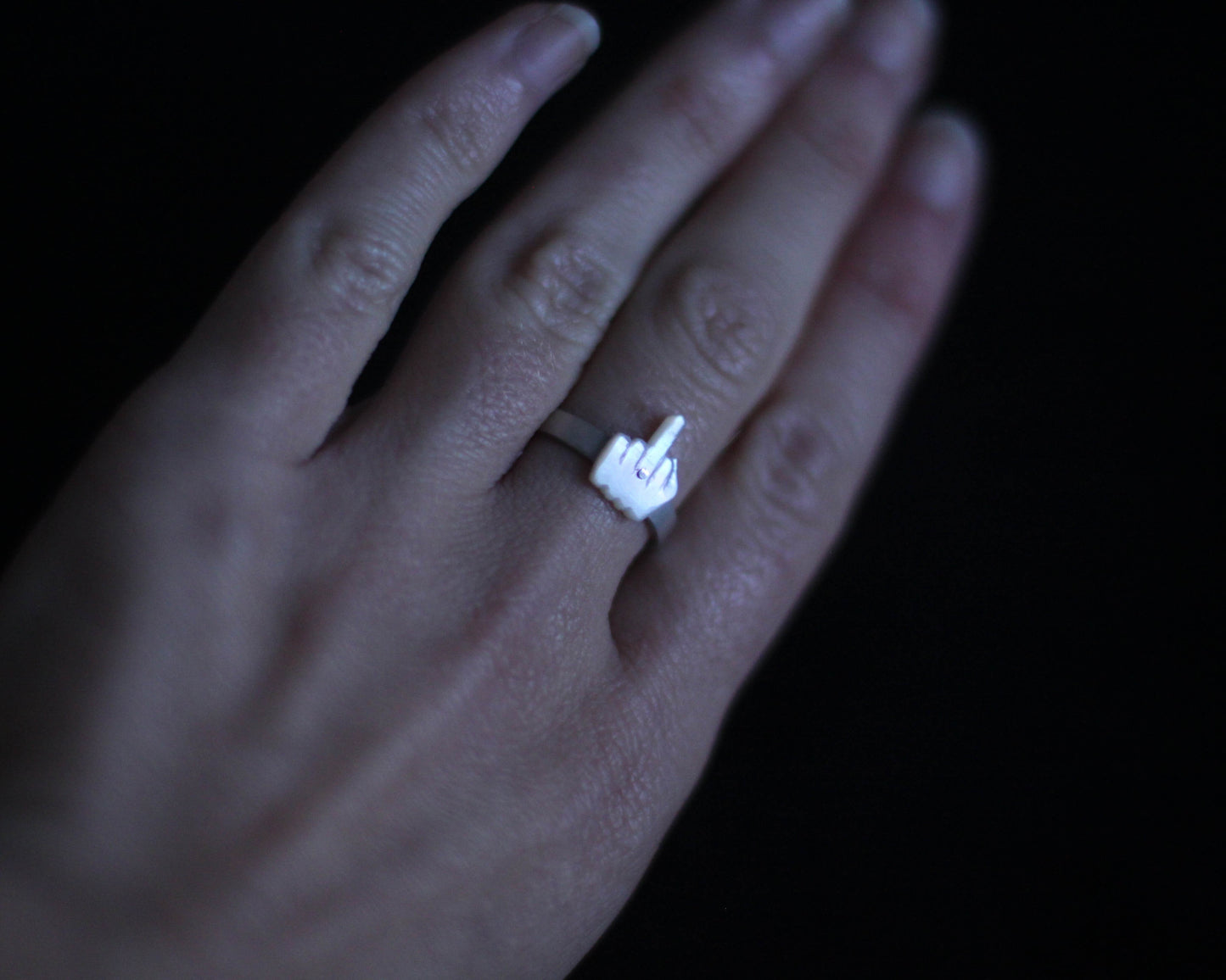 vue d'une main portant une bague en argent massif surmontée d'un doigt d'honneur en nacre