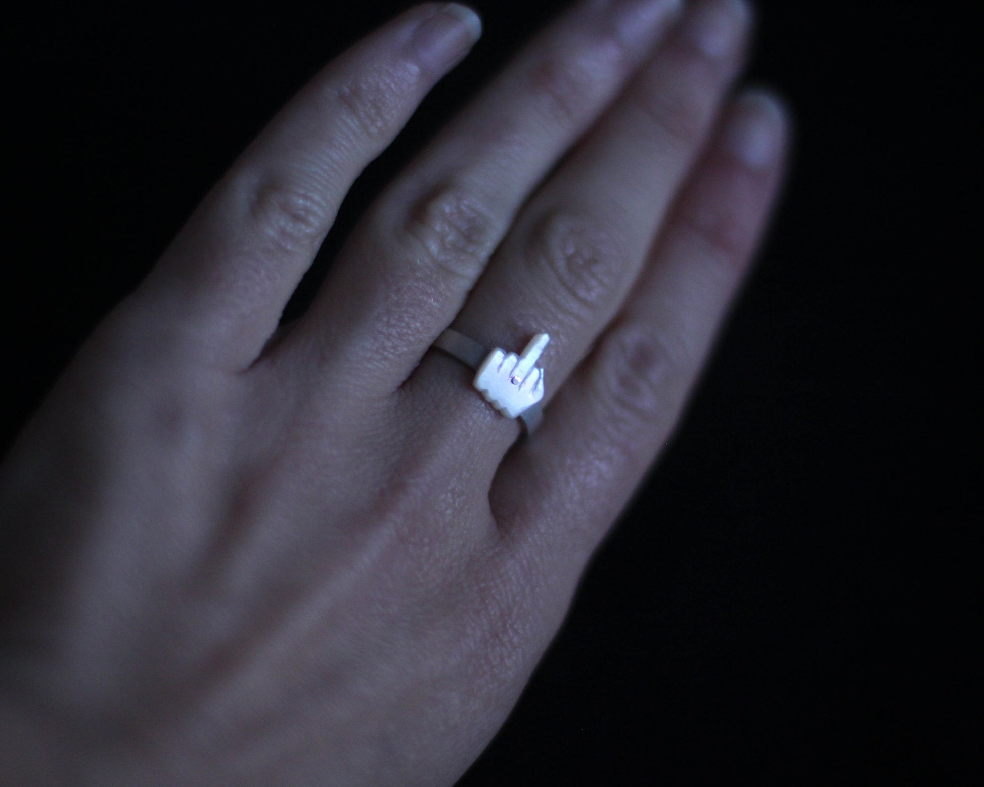 vue d'une main portant une bague en argent massif surmontée d'un doigt d'honneur en nacre