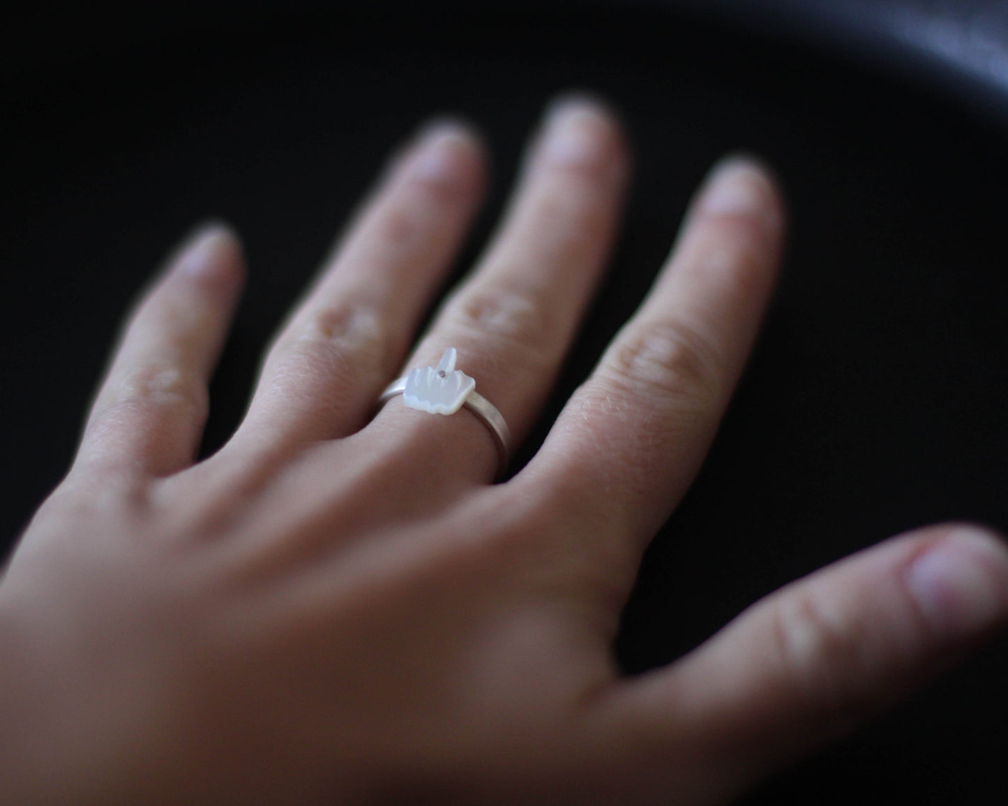 bague en argent surmontée d'un doigt d'honneur en nacre sculptée, portée au doigt