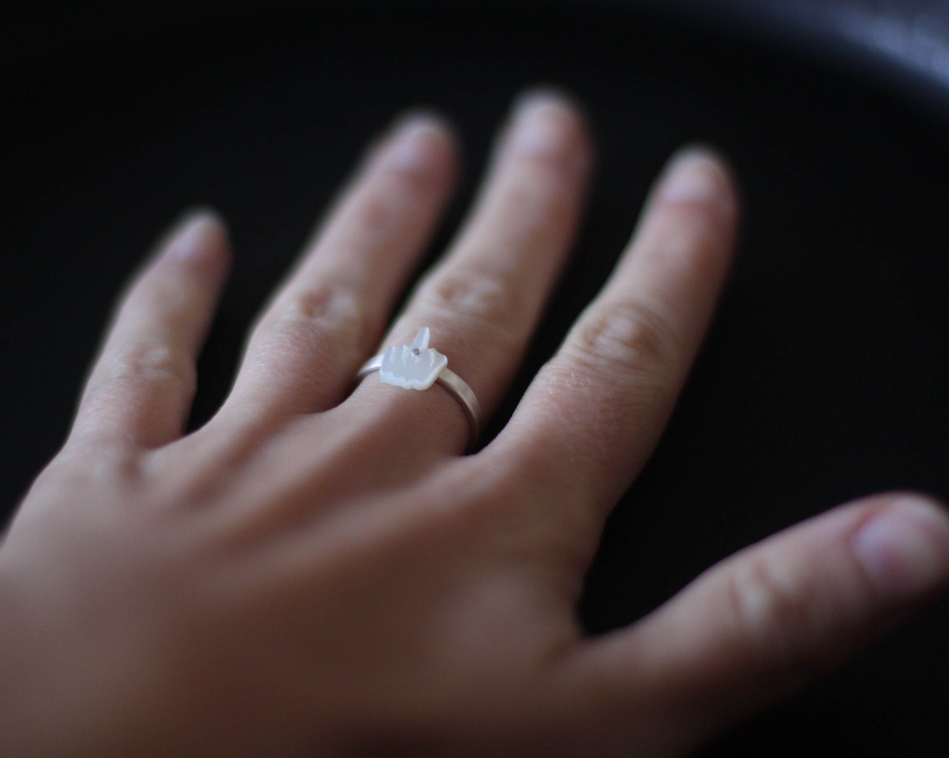 bague en argent surmontée d'un doigt d'honneur en nacre sculptée, portée au doigt