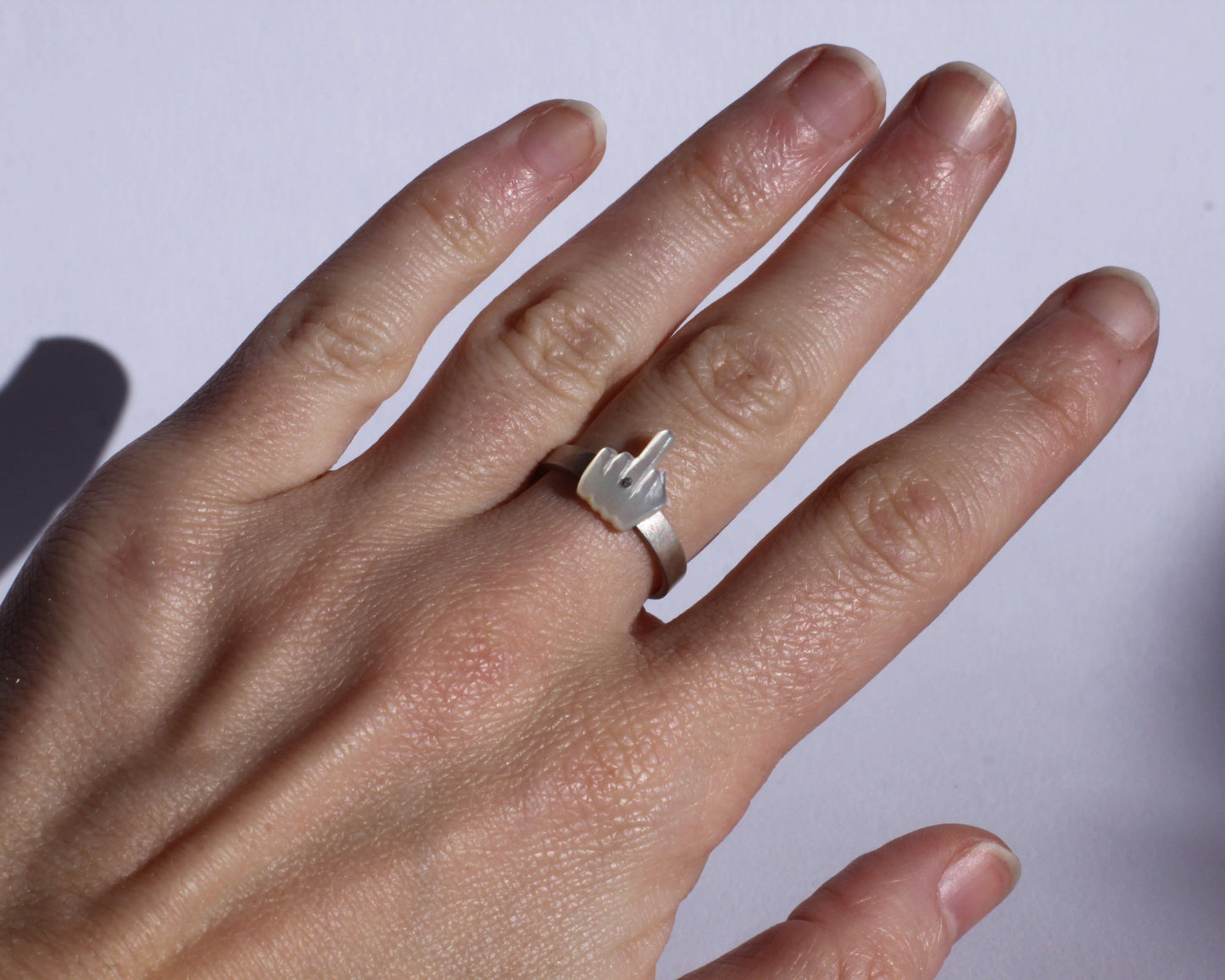 vue détaillée d'une bague en forme de doigt d'honneur, en argent massif et nacre sculptée, portée au doigt