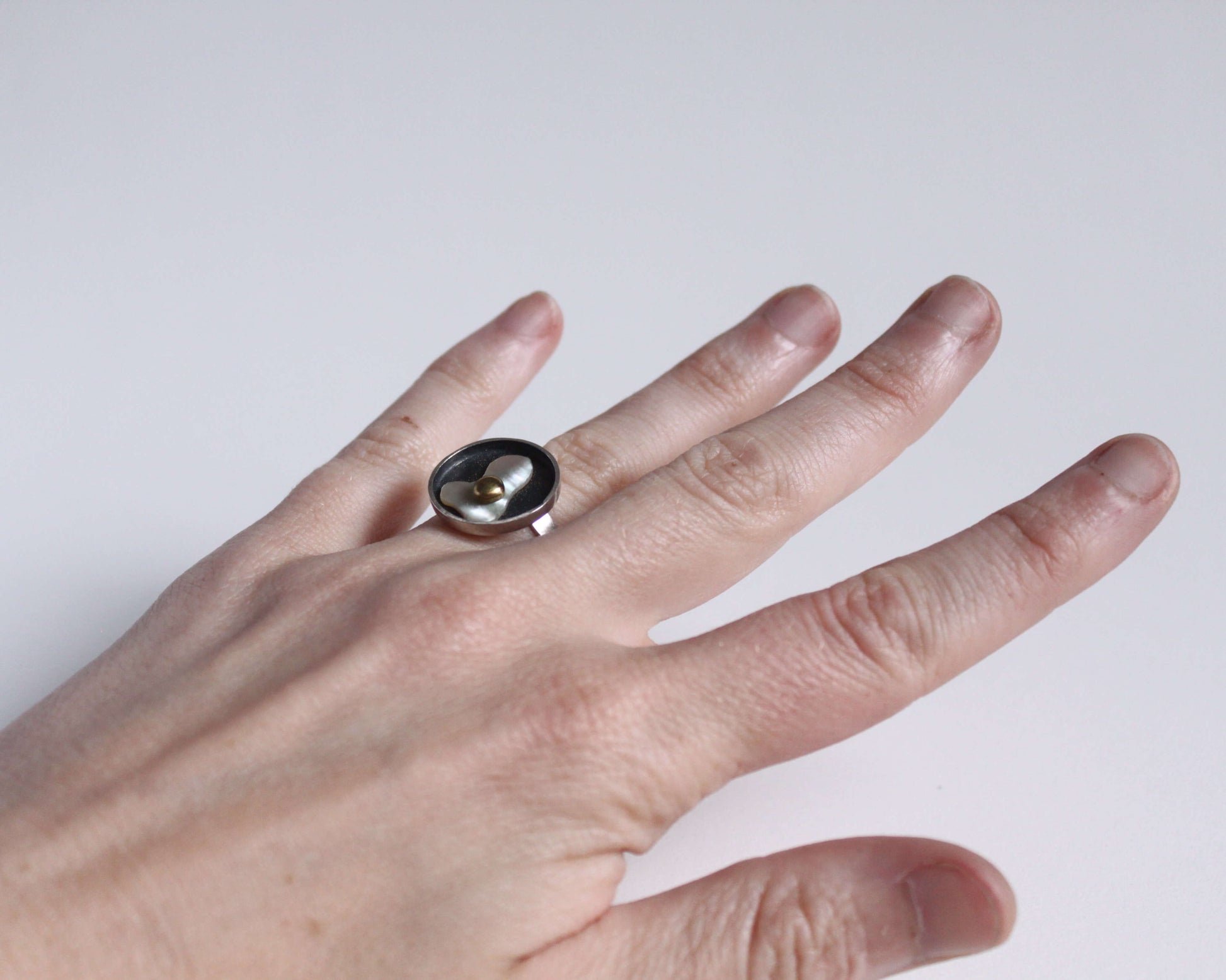 bague en argent portée au doigt représentant un oeuf au plat en nacre et en laiton dans une poêle