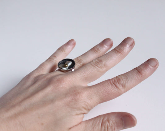 bague en argent portée au doigt représentant un oeuf au plat en nacre et en laiton dans une poêle