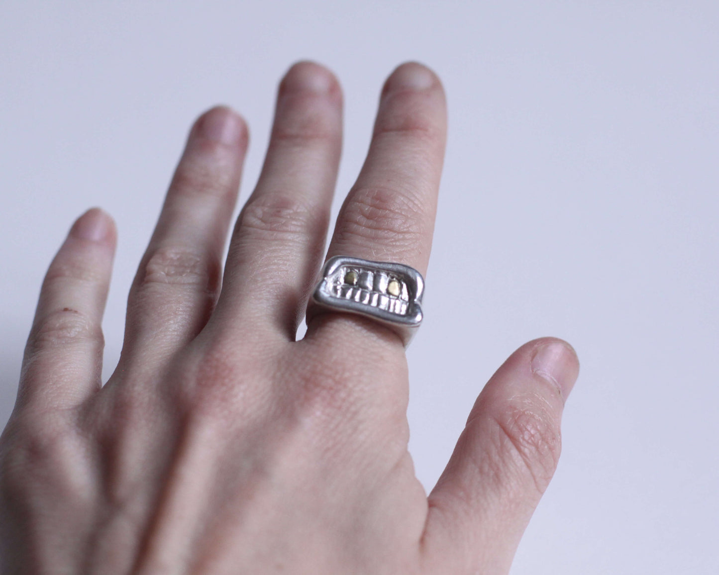 bague en argent massif représentant une bouche avec deux dents en laiton, portée au doigt