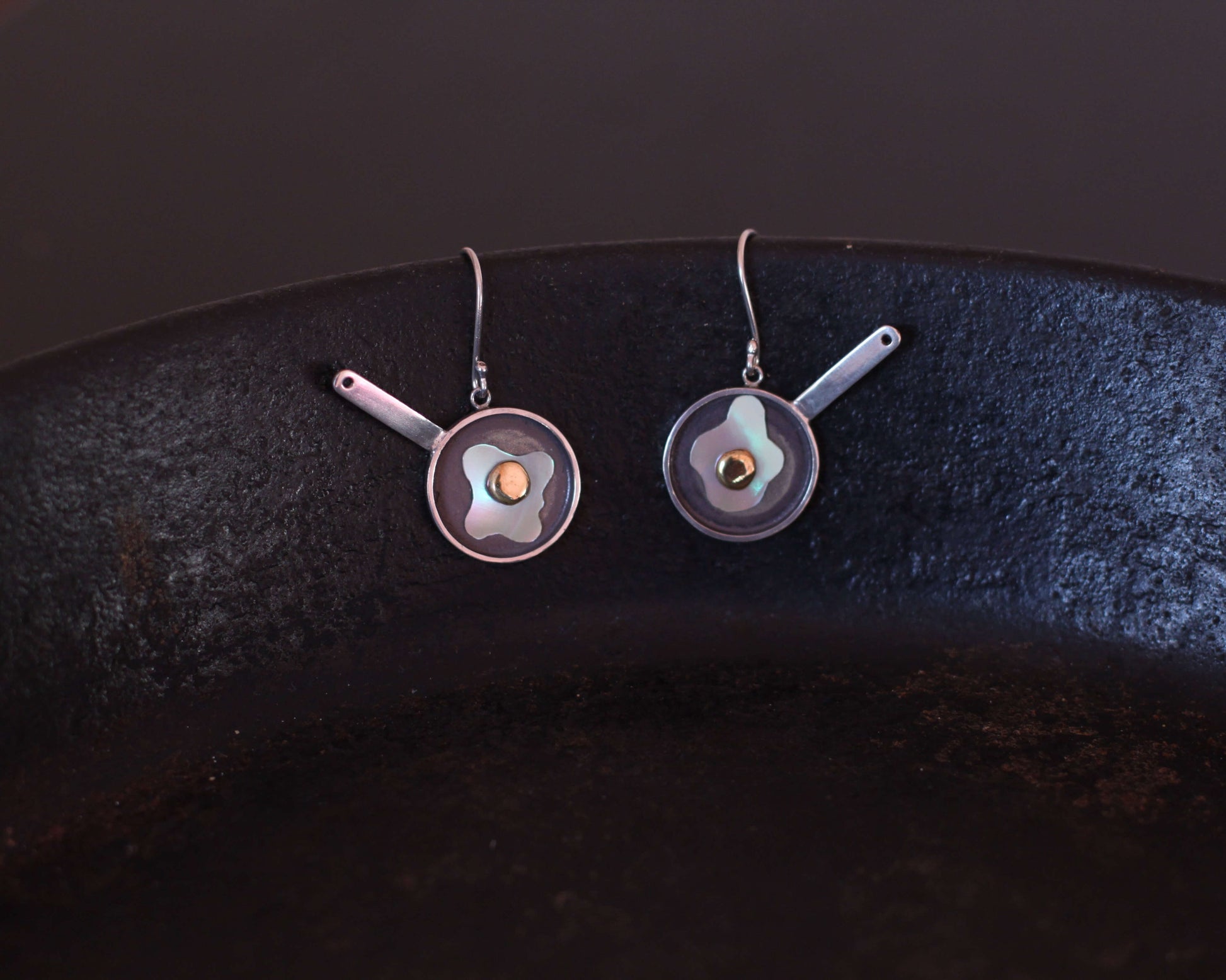 paire de boucles d'oreilles symbolisant des oeufs au plat, accrochée au rebord d'une vraie poêle