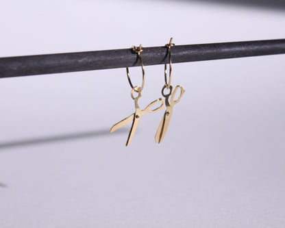 vue détaillée d'une paire de boucles d'oreilles en laiton doré représentant une paire de ciseaux