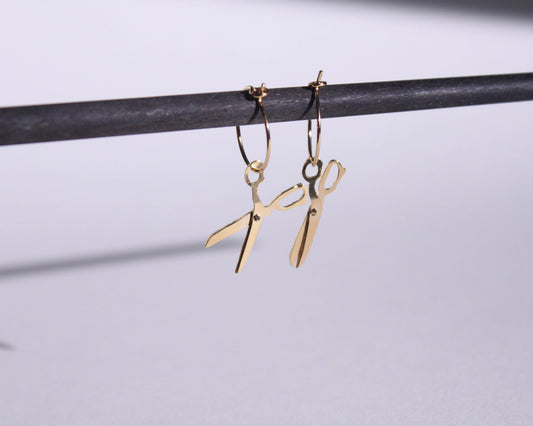 vue détaillée d'une paire de boucles d'oreilles en laiton doré représentant une paire de ciseaux