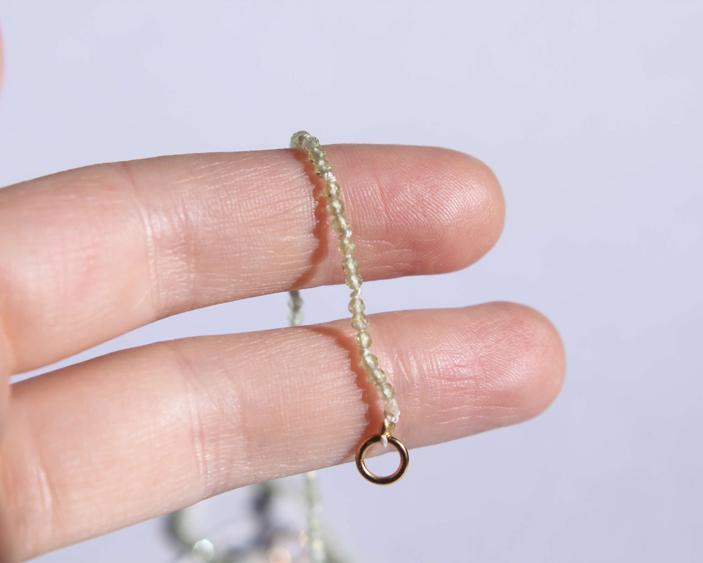 Bout du collier en perles en peridot facetté anneau tenu sur deux doigts