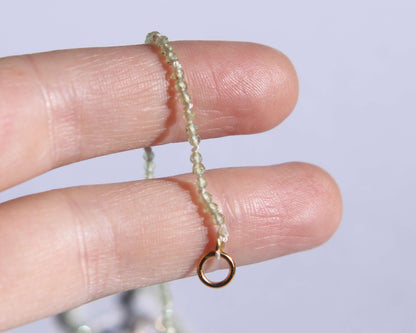 Gros zoom sur le bout du collier en perles en peridot facetté anneau tenu sur deux doigts 