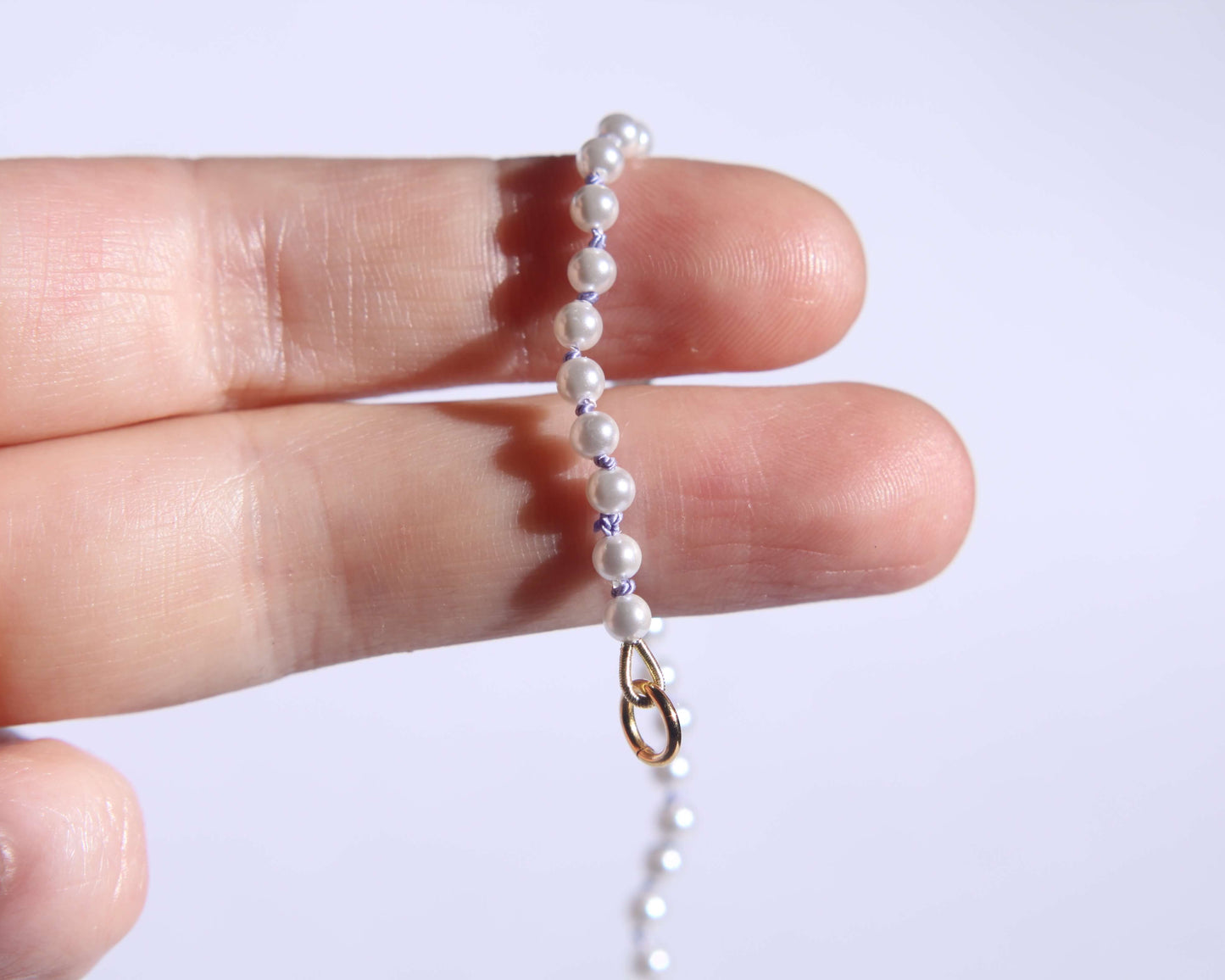 Collier en perles avec noeuds en fil de soie lila tenu sur deux doigts avec anneau visible