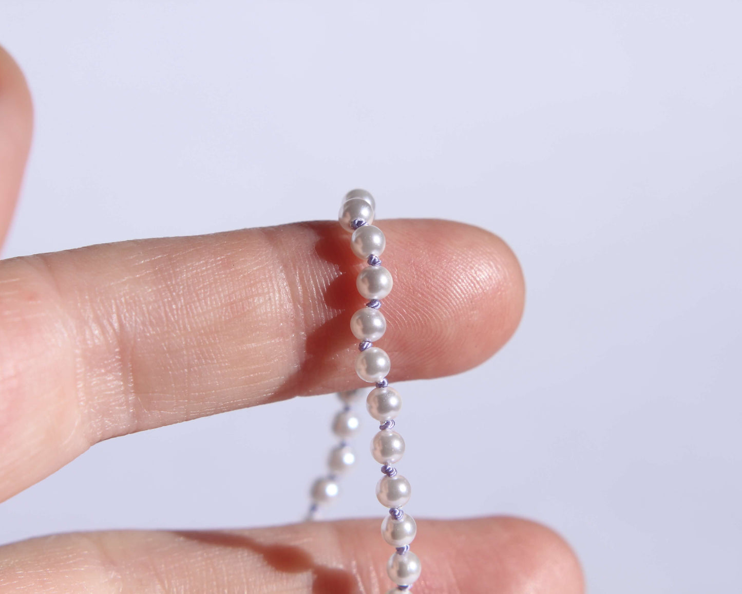 Collier en perles avec noeuds en fil de soie lila tenu sur deux doigts