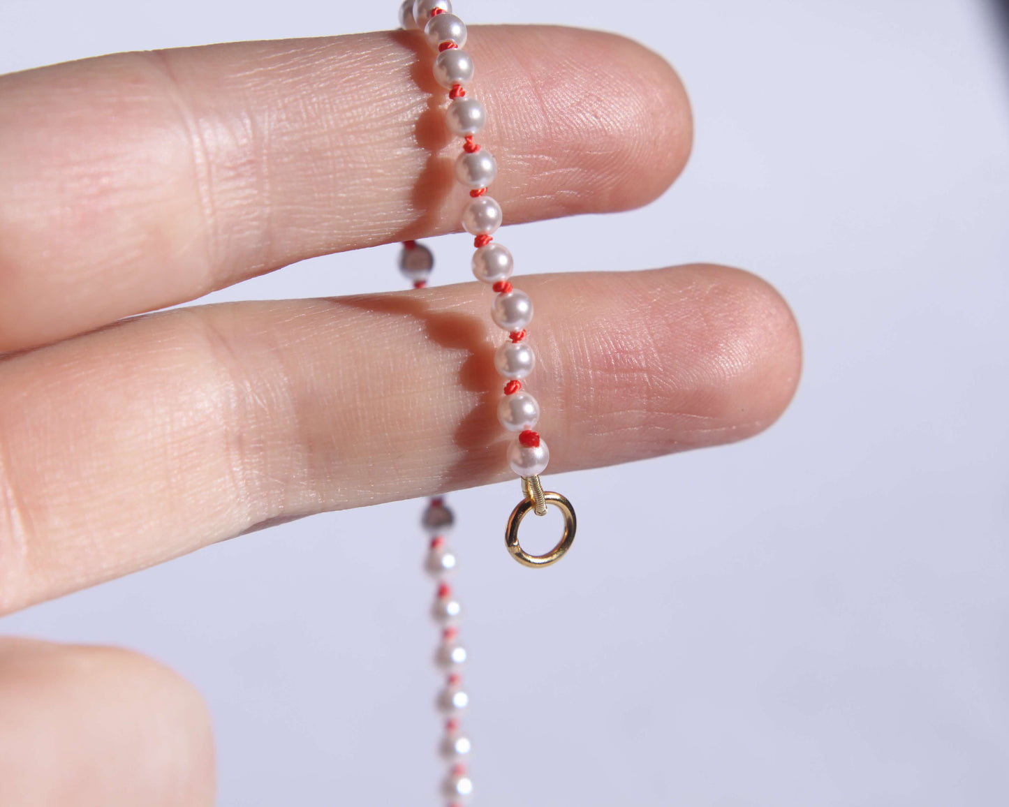 Collier en perles avec noeuds en fil de soie orange tenu sur deux doigts avec anneau visible