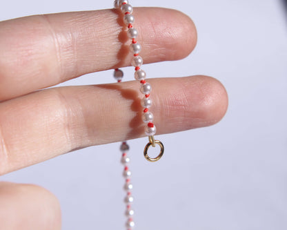 Collier en perles avec noeuds en fil de soie orange tenu sur deux doigts avec anneau visible