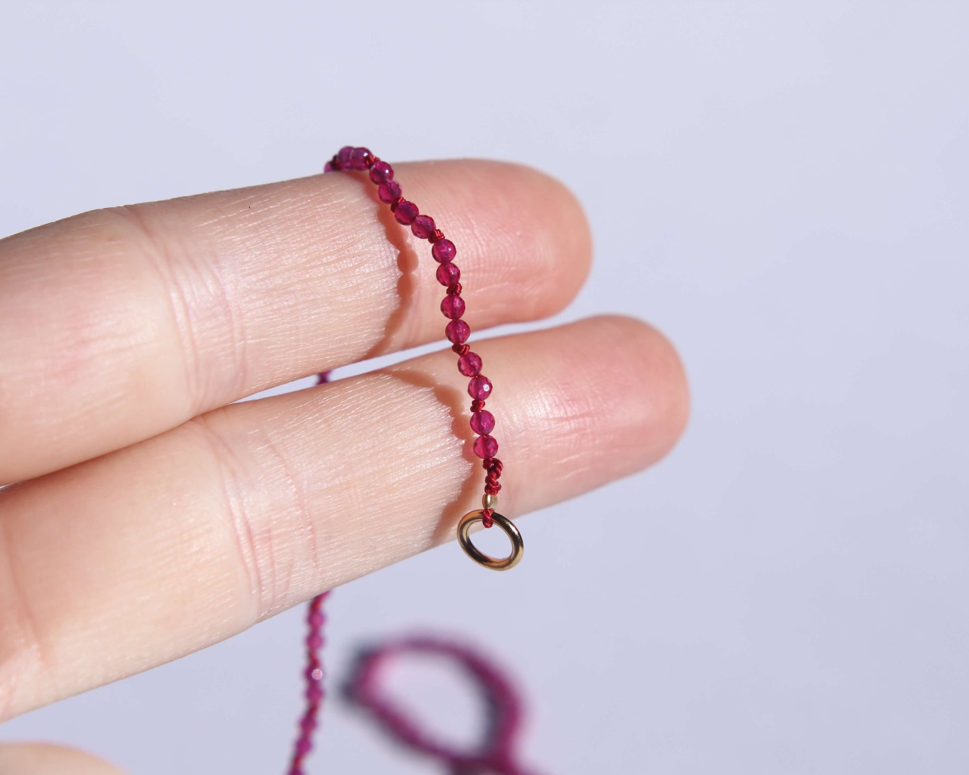 Bout du collier en perles en rubis chauffé facetté anneau tenu sur deux doigts