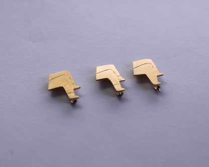 trois broches représentant des petites jambes croisées ou l'une a des poils et des chaussettes, l'une a juste des chaussettes et la dernière des poils vues d'en bas