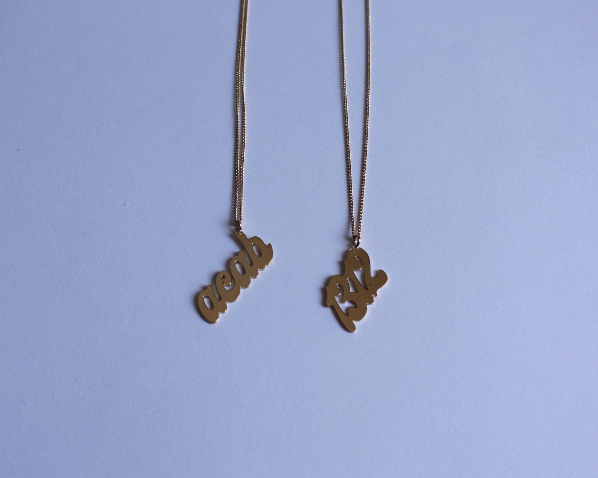 deux pendentifs en laiton doré représentant le mot "acab" et le nombre "1312"