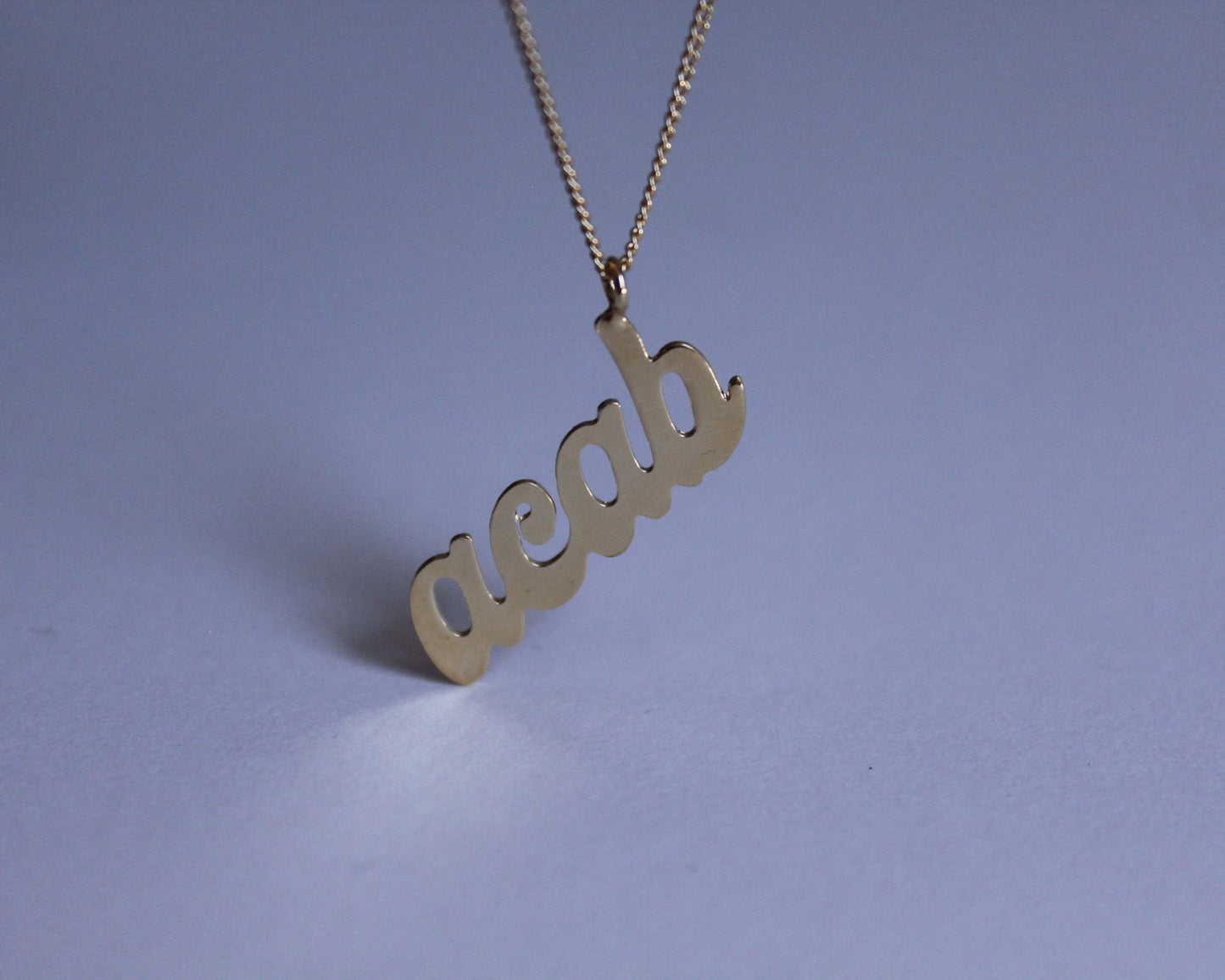 zoom sur un pendentif en laiton doré représentant le mot "acab"