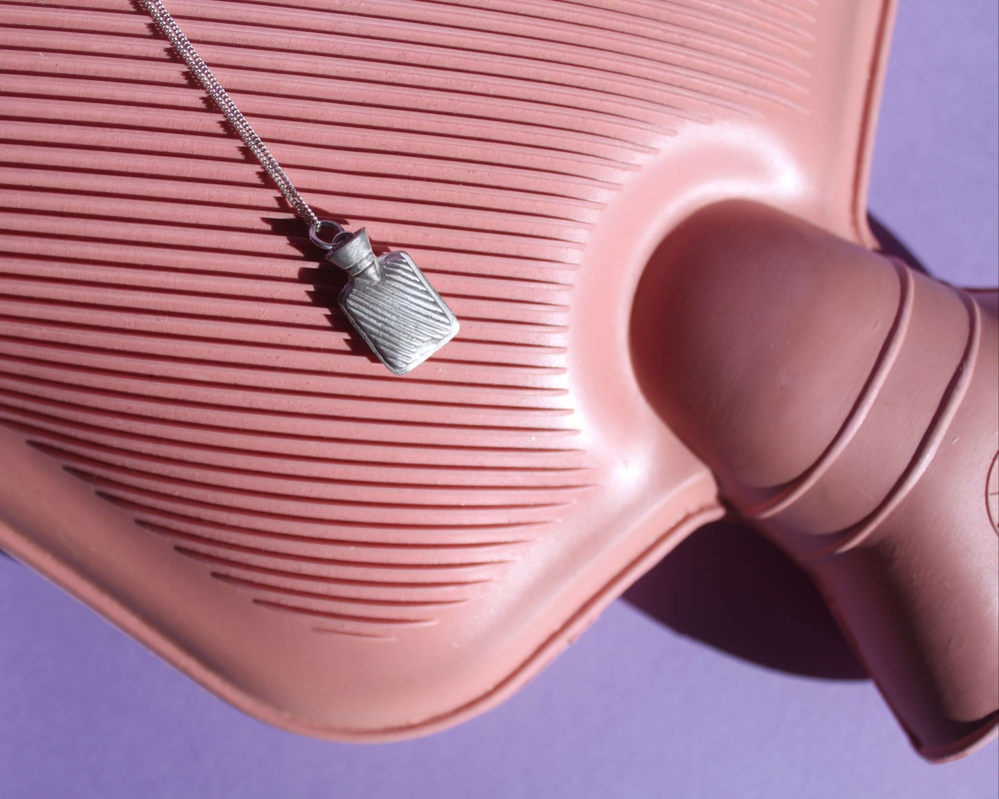 pendentif en argent massif évoquant une bouillotte, posé sur une véritable bouillotte