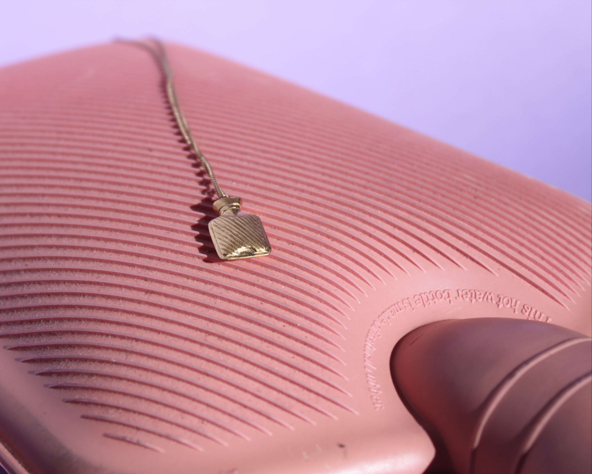 collier avec un pendentif en forme de bouillotte en laiton plaqué or posé sur une vraie bouillotte