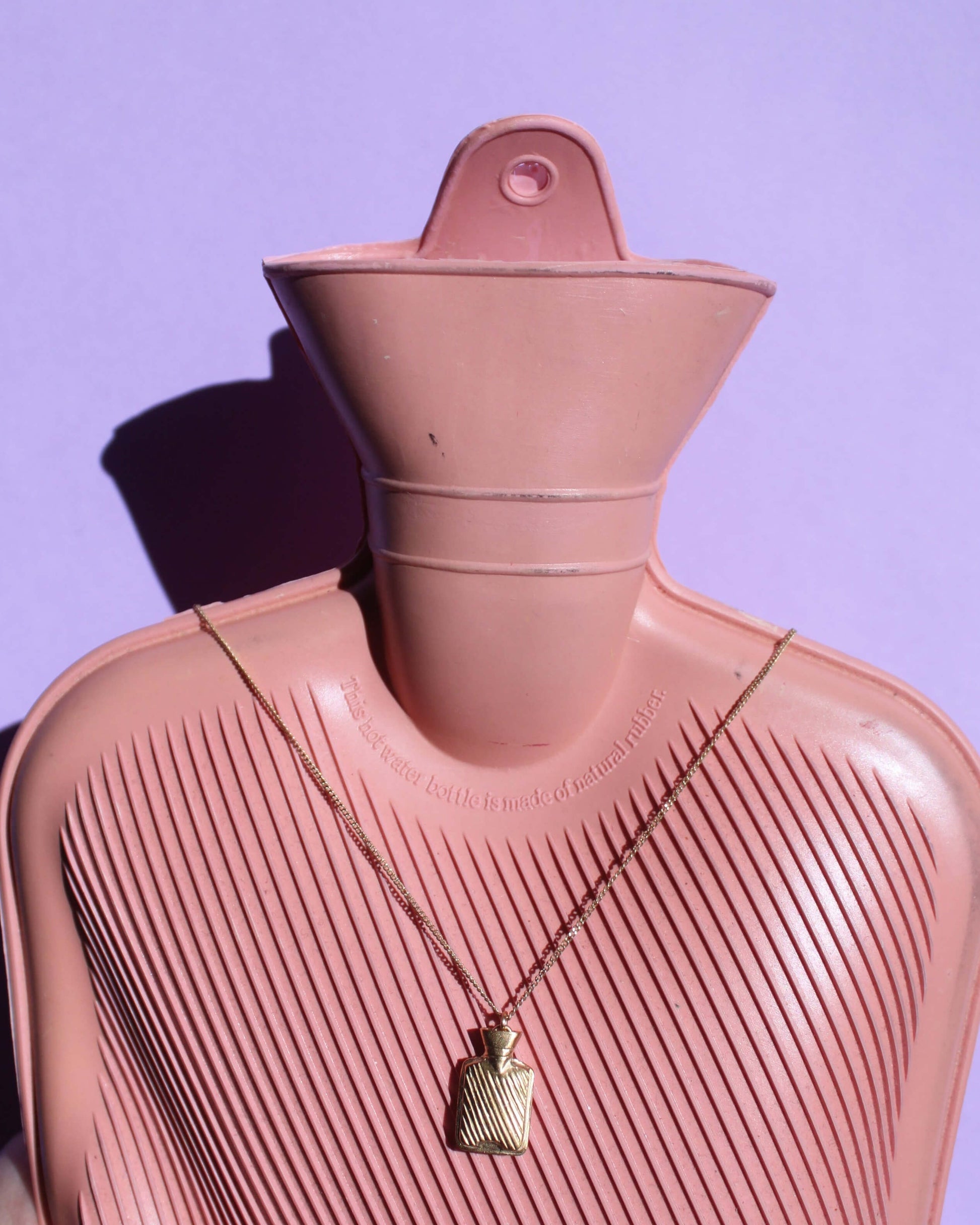 vue de face d'un collier avec un pendentif en laiton plaqué or en forme de bouillotte accroché à une véritable bouillotte