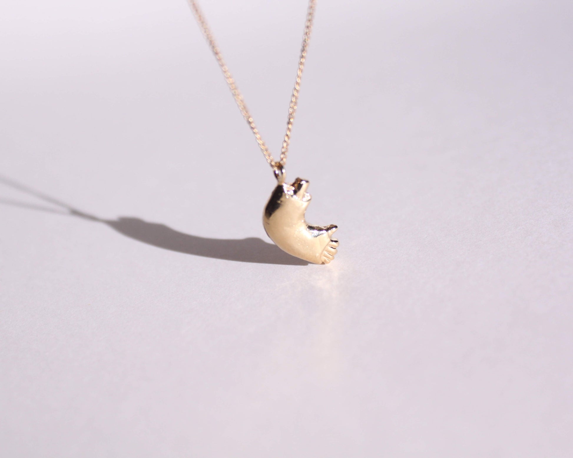 pendentif en laiton plaqué or représentant un bras cassé