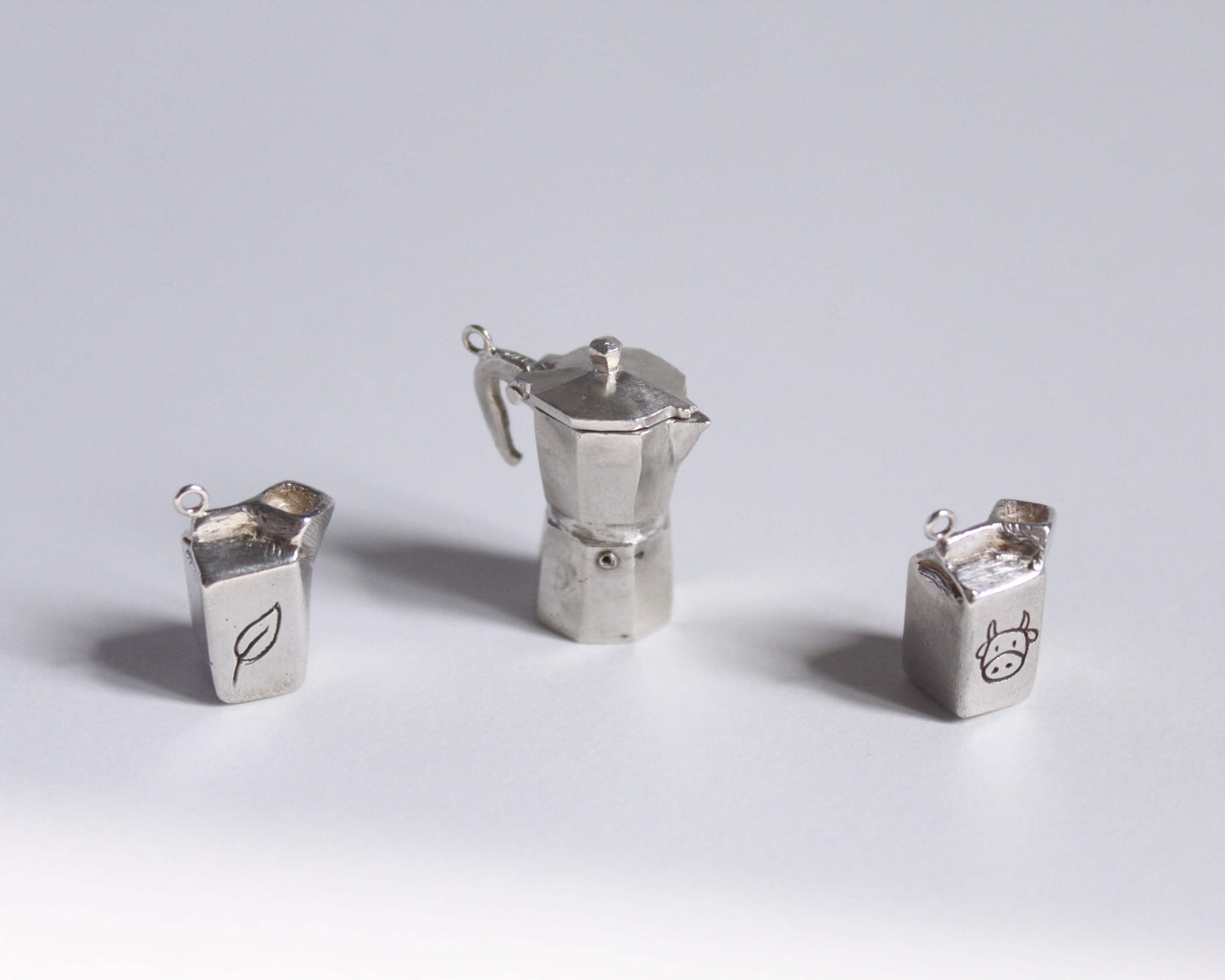 un pendentif en argent massif représentant une cafetière italienne accompagné de deux petits pendentifs en forme de briques de lait