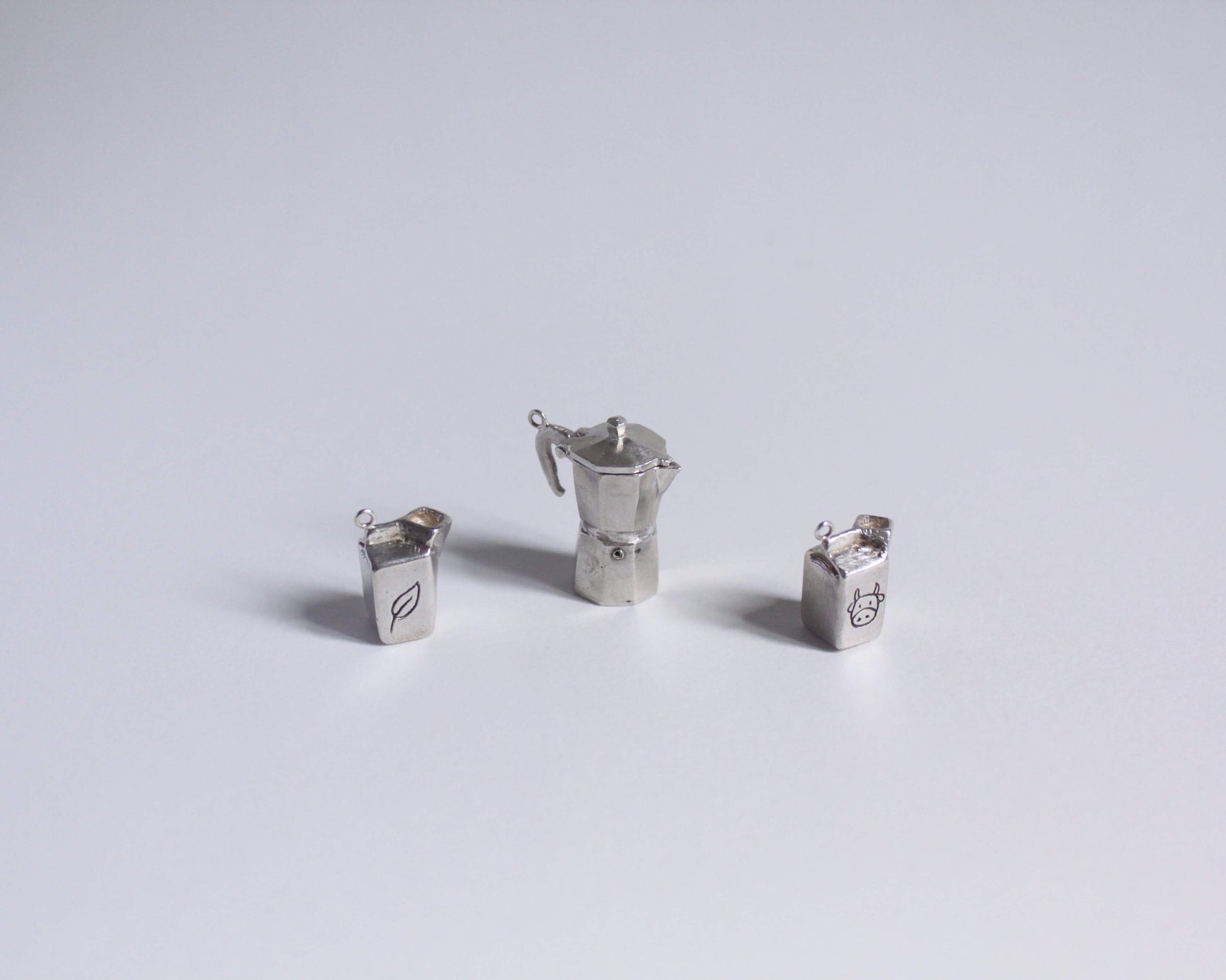 deux pendentifs en argent en forme de briques de lait accompagnés d'un pendentif en forme de cafetière italienne