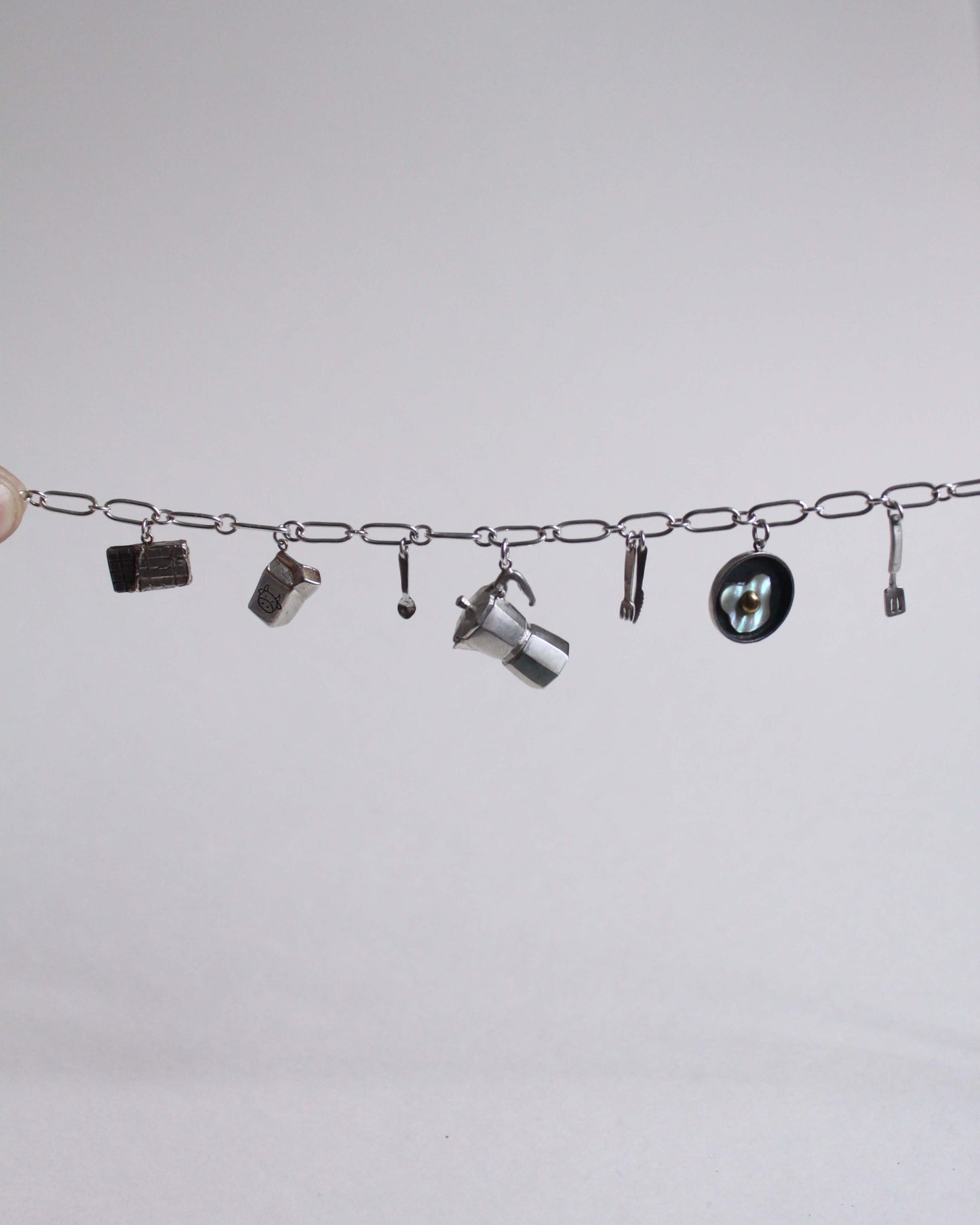 une chaine à laquelle sont accrochés différents pendentifs en argent sur le thème du petit déjeuner