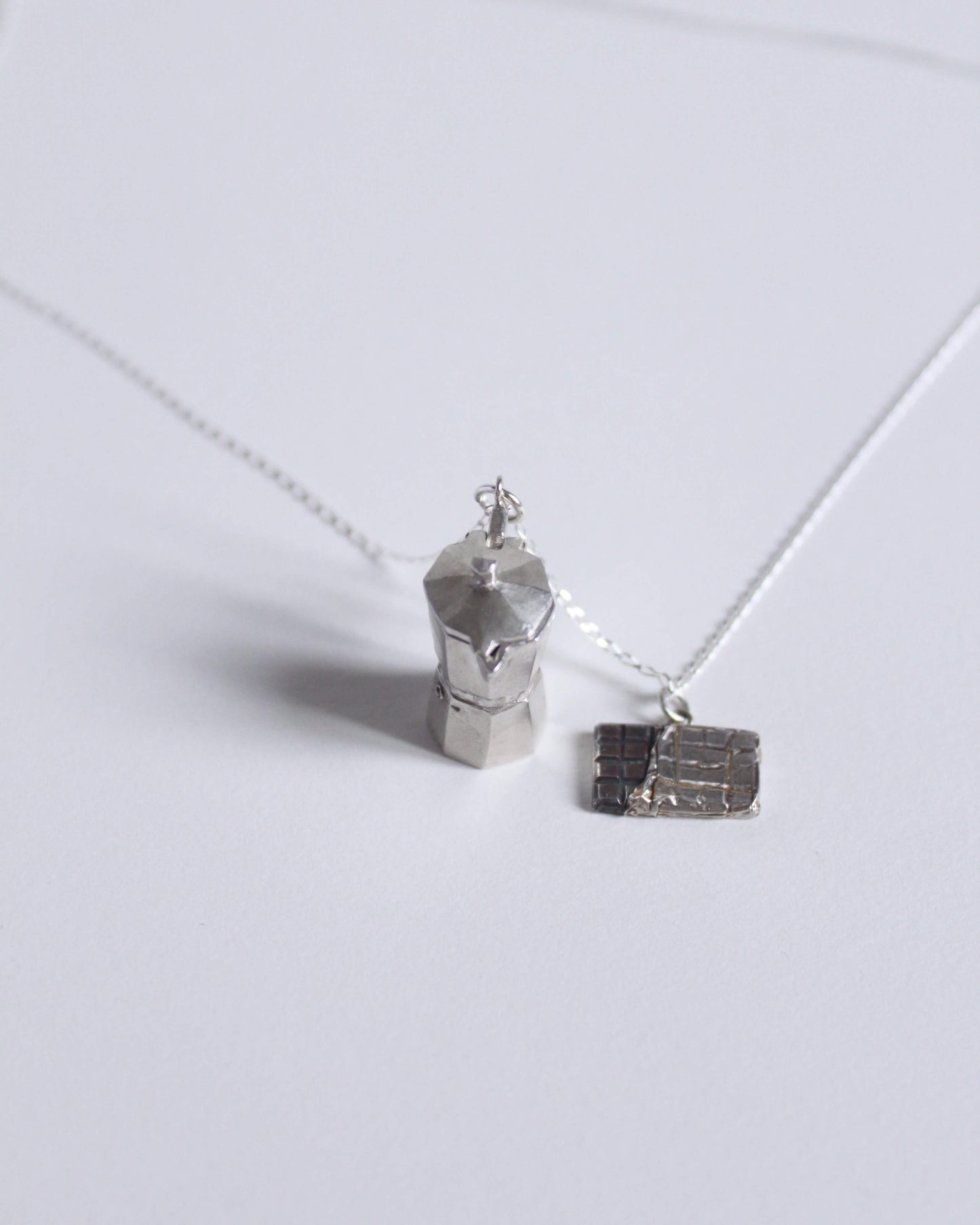 une chaine a laquelle est accroché un pendentif en argent massif en forme de cafetière italienne et un pendentif représentant une tablette de chocolat