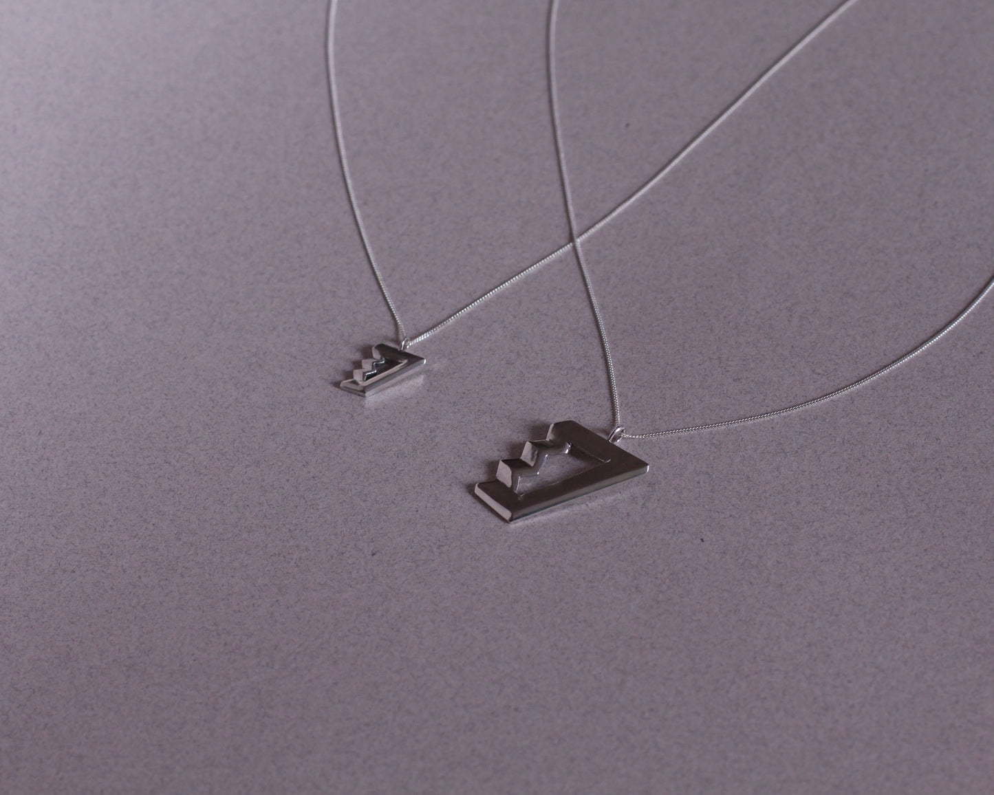 deux colliers avec des pendentifs en argent massif symbolisant des escaliers de penrose