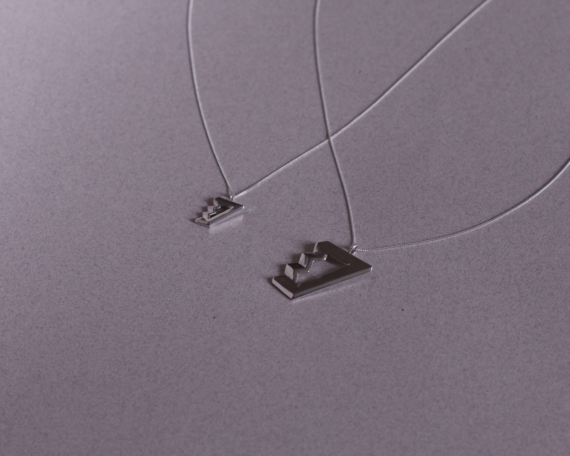 deux colliers avec des pendentifs en argent massif symbolisant des escaliers de penrose