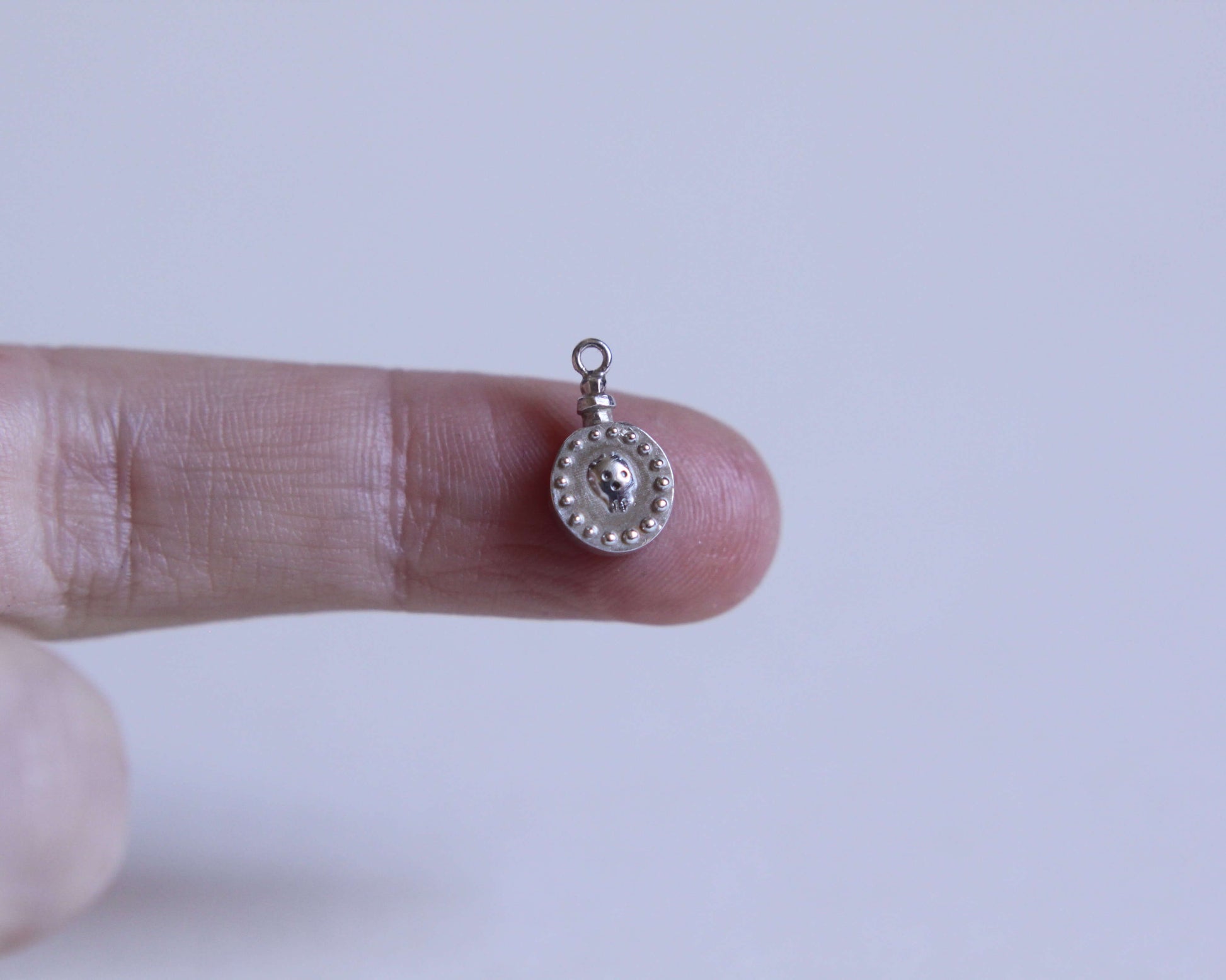 zoom sur un pendentif rond en forme de fiole de poison avec un crâne dessus