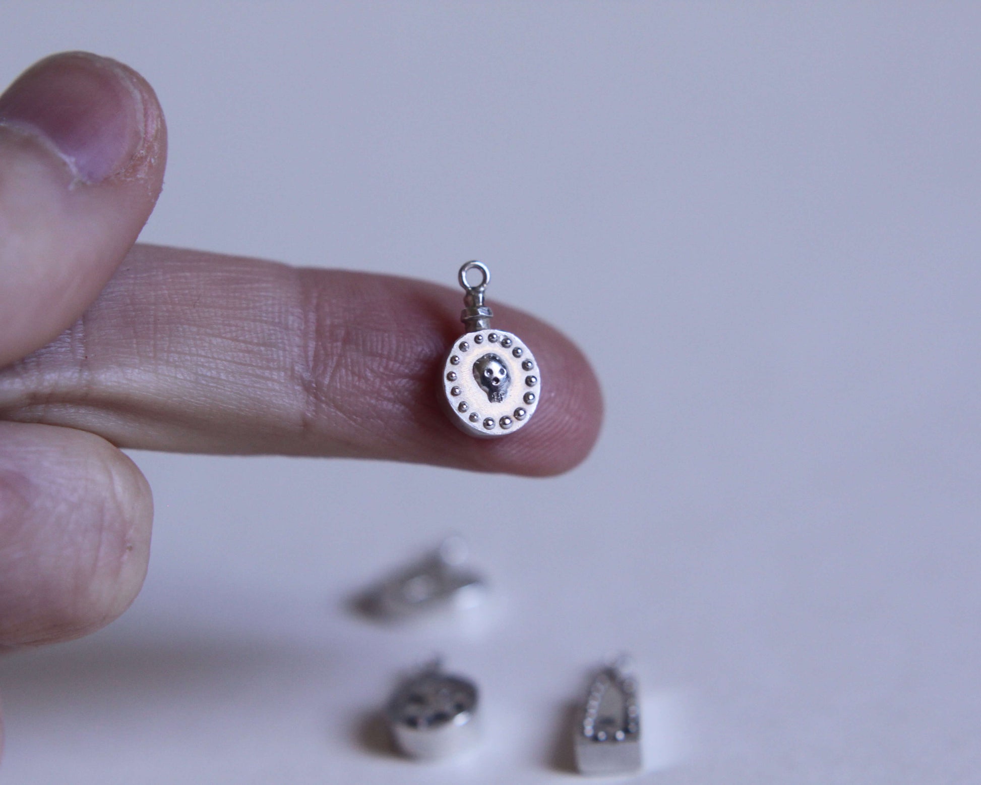 pendentif rond en argent représentant une  fiole de poison avec un crâne dessus