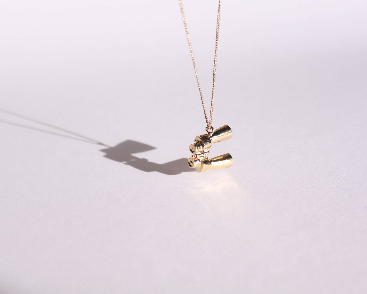 pendentif en laiton plaqué or symbolisant une paire de jumelles, suspendu au bout d'une chaine