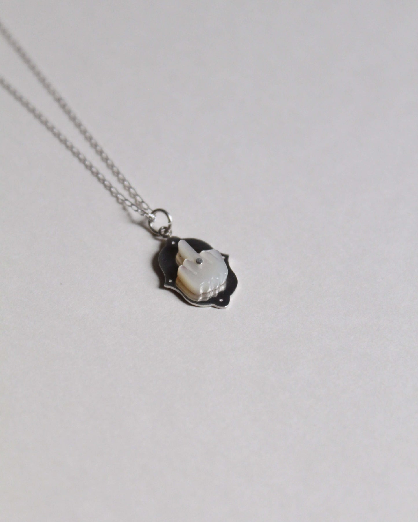 pendentif représentant un doigt d'honneur en nacre sculptée sur argent