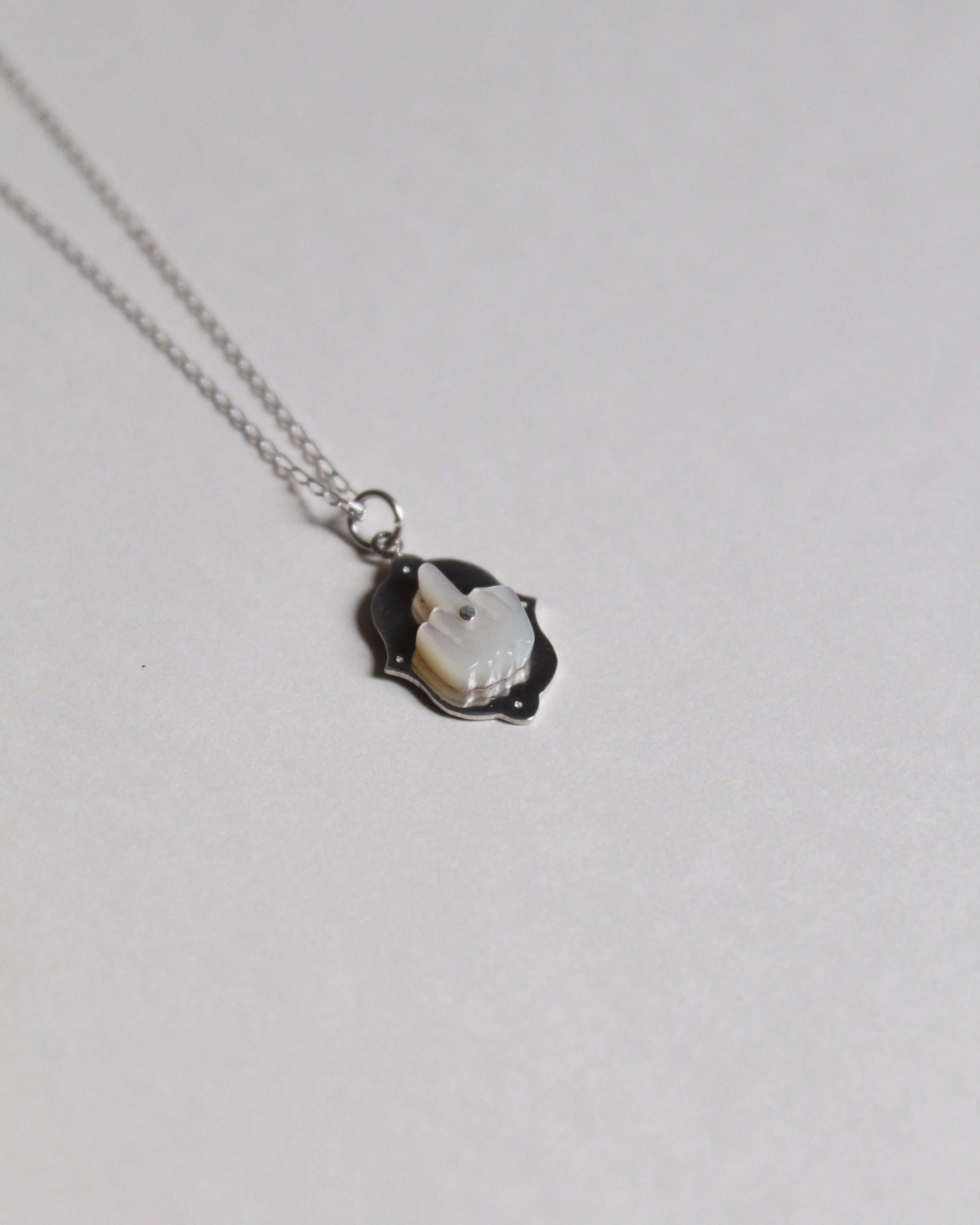 pendentif représentant un doigt d'honneur en nacre sculptée sur argent