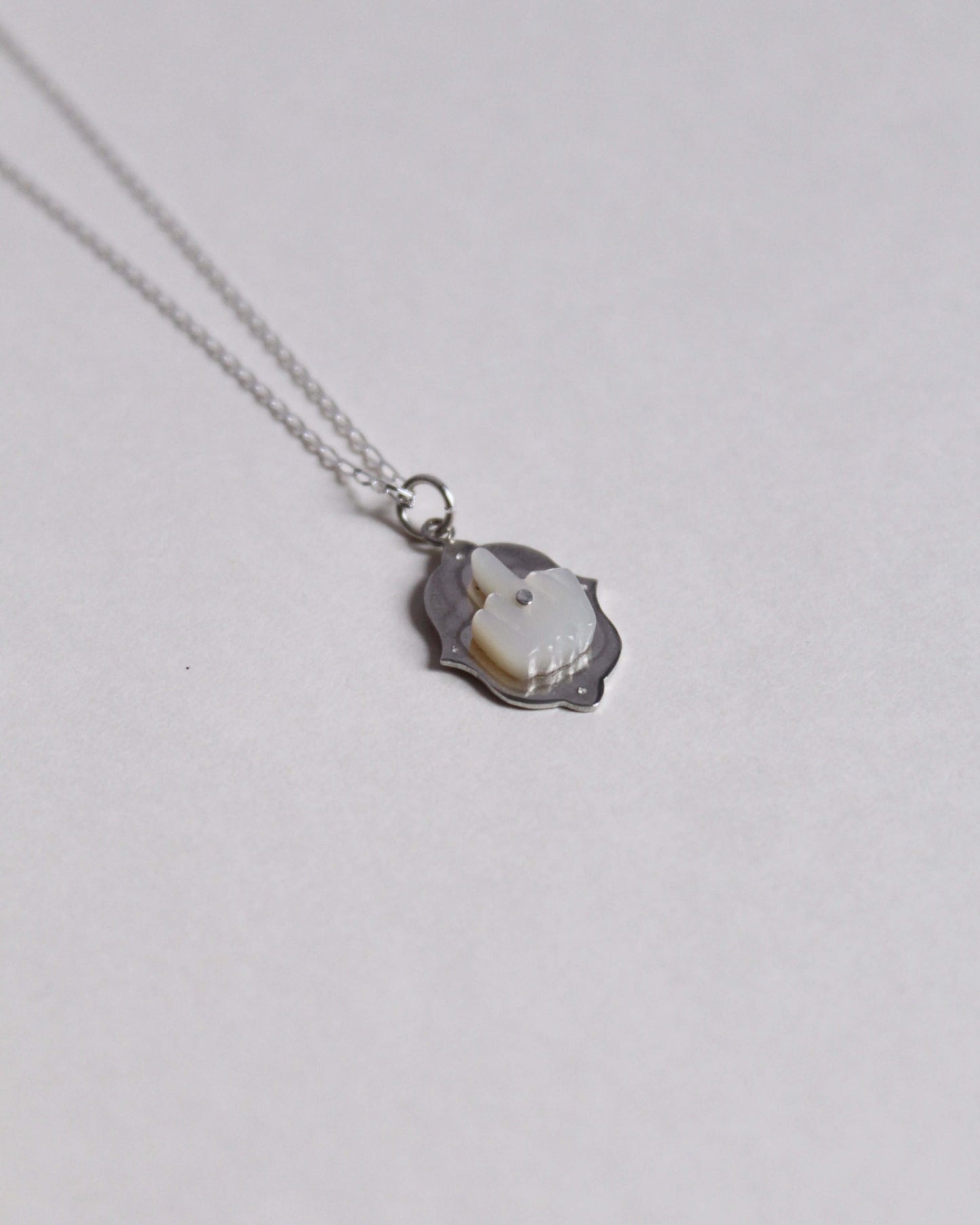 pendentif en argent surmonté d'un doigt d'honneur en nacre sculptée au bout d'une chaine