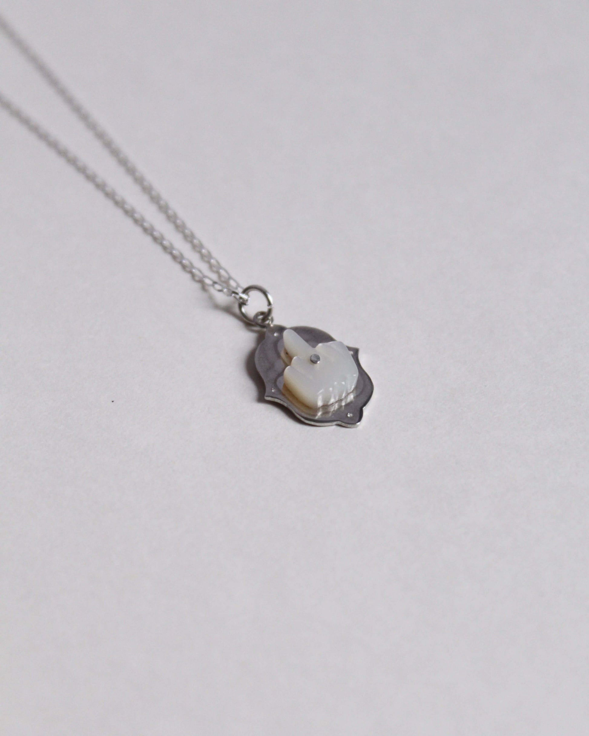 pendentif en argent surmonté d'un doigt d'honneur en nacre sculptée au bout d'une chaine