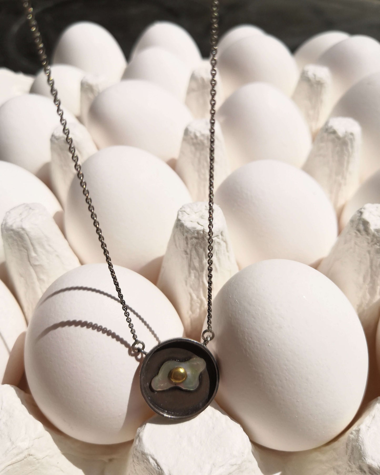 pendentif en forme d'oeuf au plat dans une poêle posé sur des oeufs