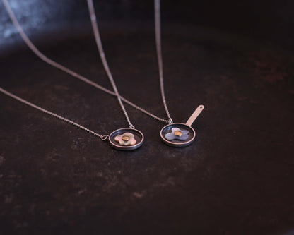 deux colliers avec des pendentifs représentant des oeufs au plat fabriquées en argent, nacre et laiton