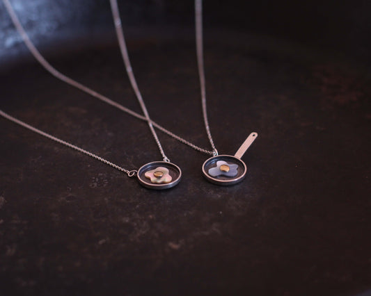 deux colliers avec des pendentifs représentant des oeufs au plat fabriquées en argent, nacre et laiton