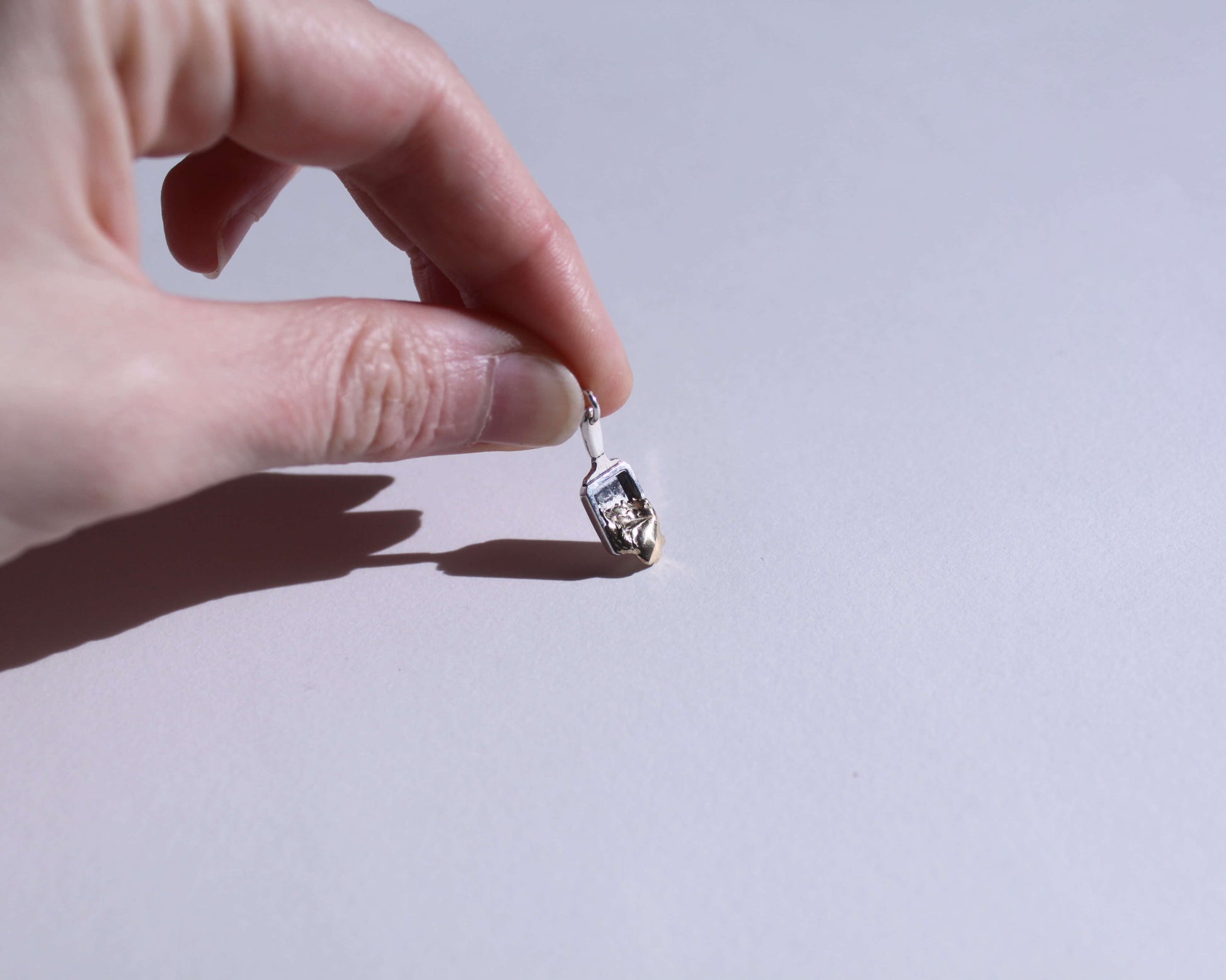 pendentif en argent représentant un poêlon à raclette avec du fromage qui coule en laiton