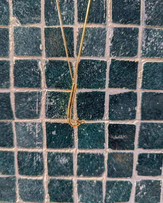 collier avec un pendentif en laiton plaqué or en forme de tuba devant un mur à carreaux