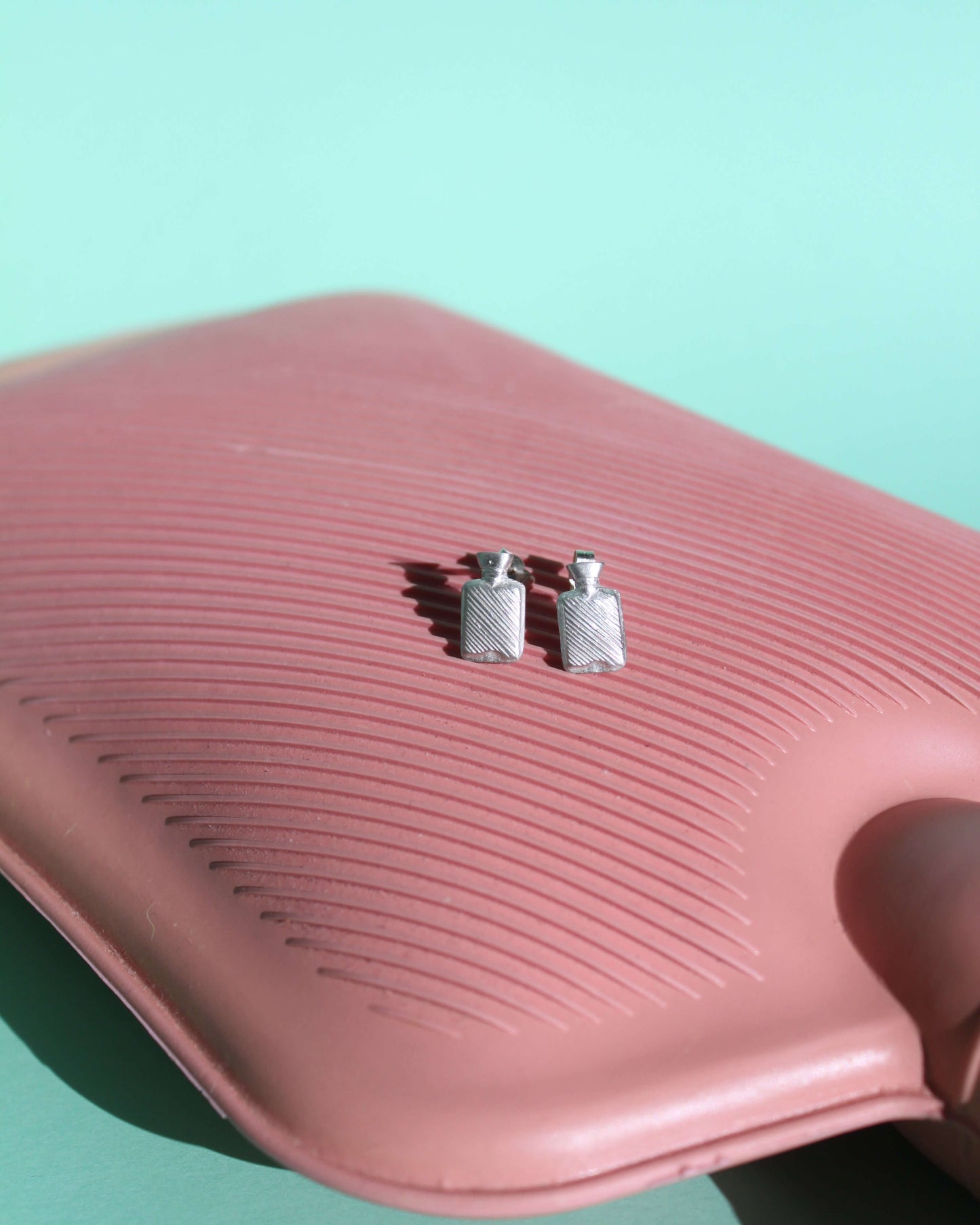 boucles d'oreilles en argent massif en formes de bouillottes, posées sur une vraie bouillotte